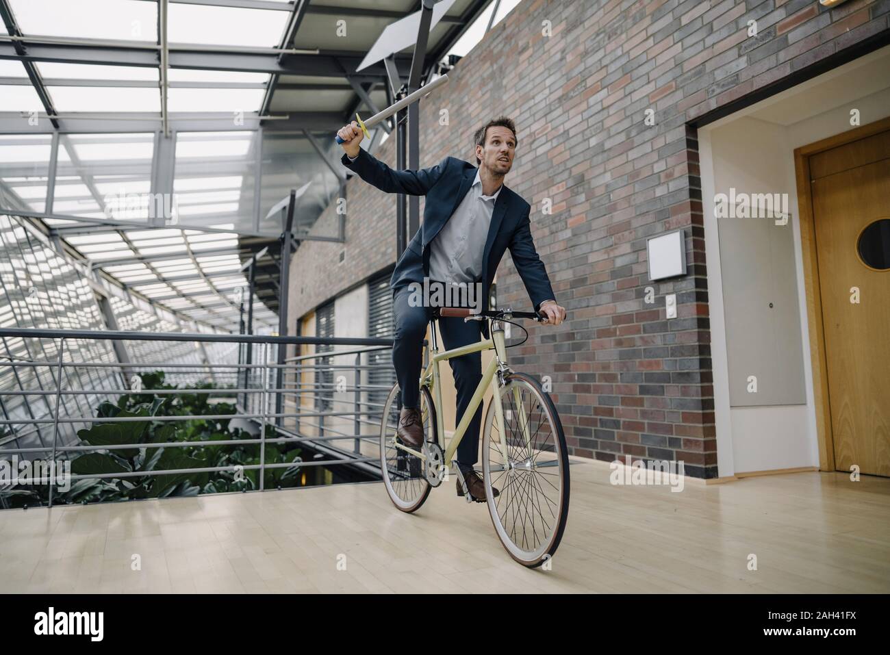 Businessman holding a toy sword and riding bicycle in modern office building Stock Photo