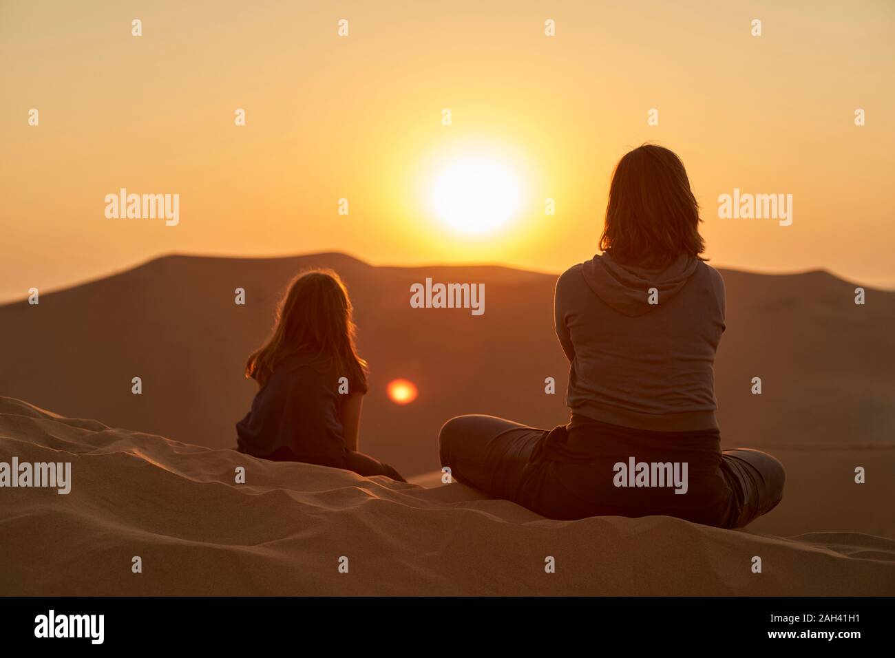 Muother and daughter sitting in desert dunes at sunset, Dune 7, Walvis Bay, Namibia Stock Photo