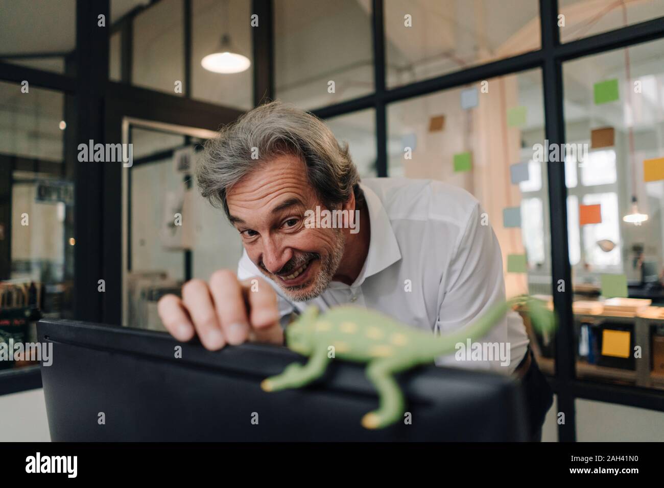 Happy senior businessman with chameleon figurine in office Stock Photo