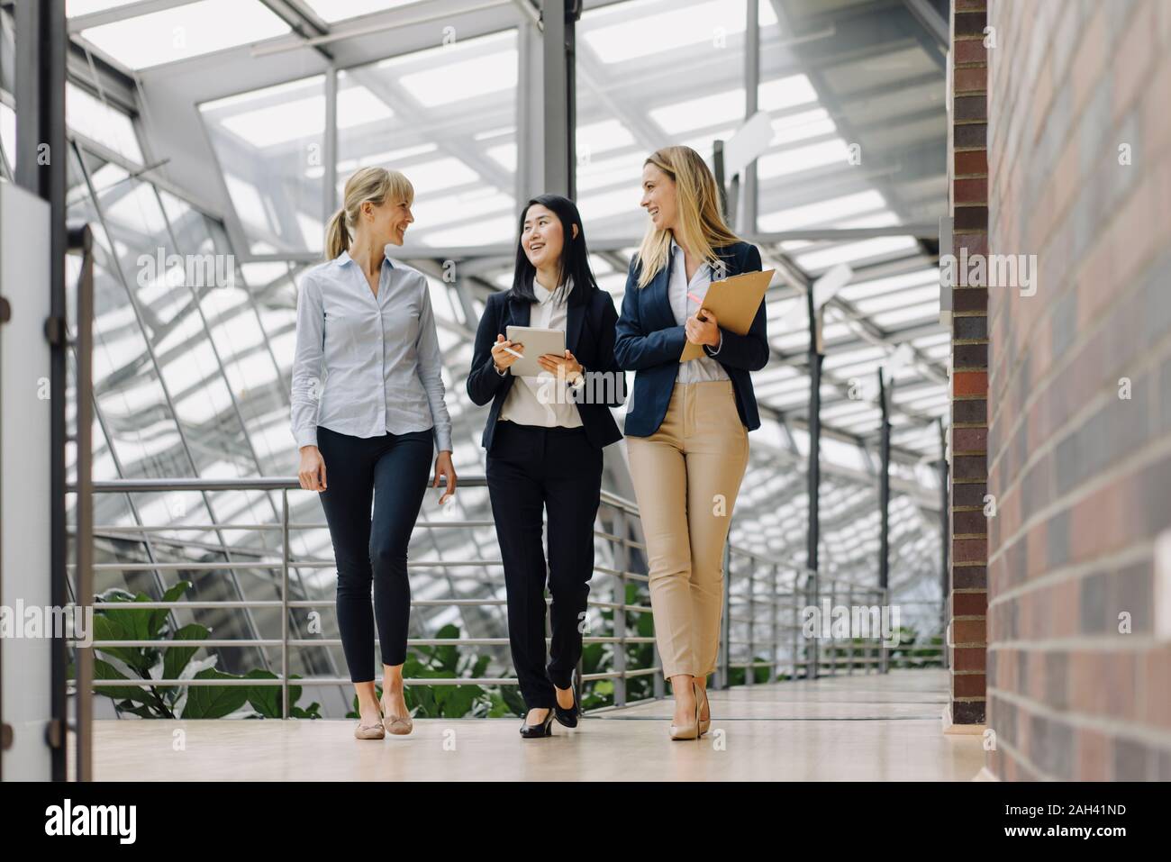 Three businesswomen with tablet walking and talking in modern office building Stock Photo