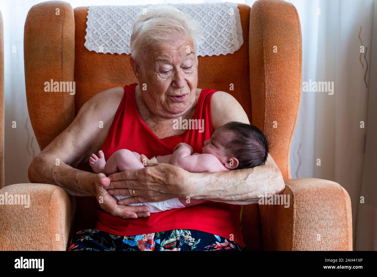Grandmother holding her newborn baby granddaughter at home Stock Photo