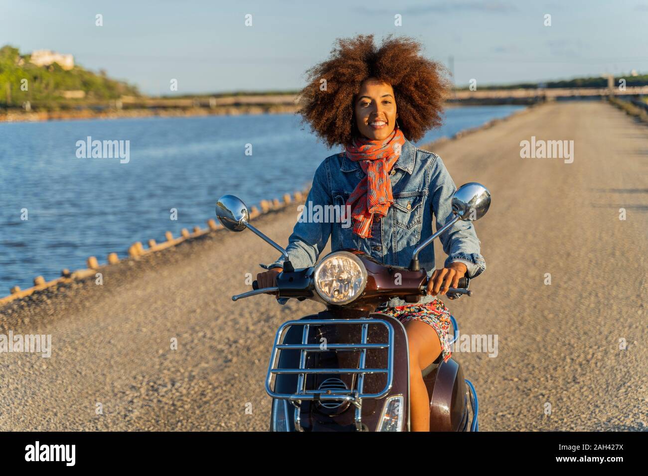 Young woman riding motor scooter on a road, Ibiza Stock Photo