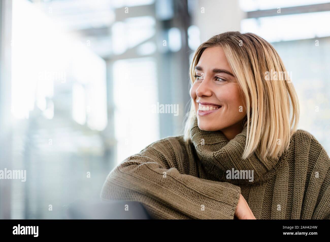 Smiling young woman sitting in waiting area looking around Stock Photo