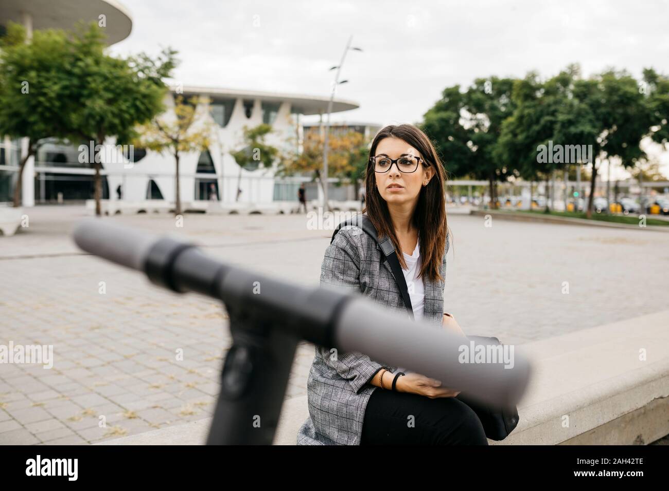 Young businesswoman with e-scooter in the city, looking sideways Stock Photo