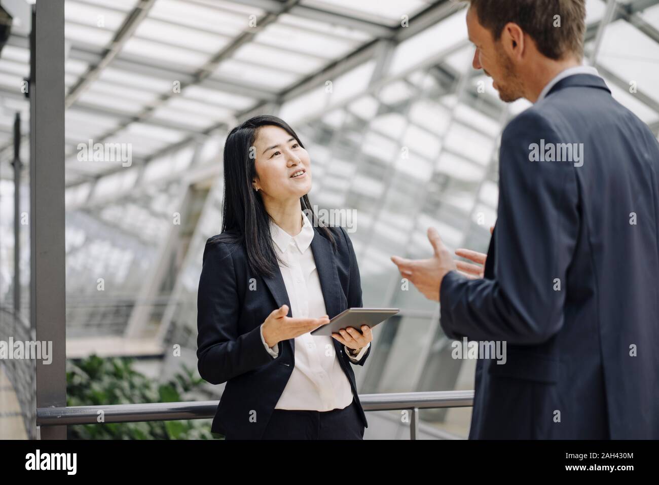 Businessman and businesswoman with tablet talking in modern office building Stock Photo