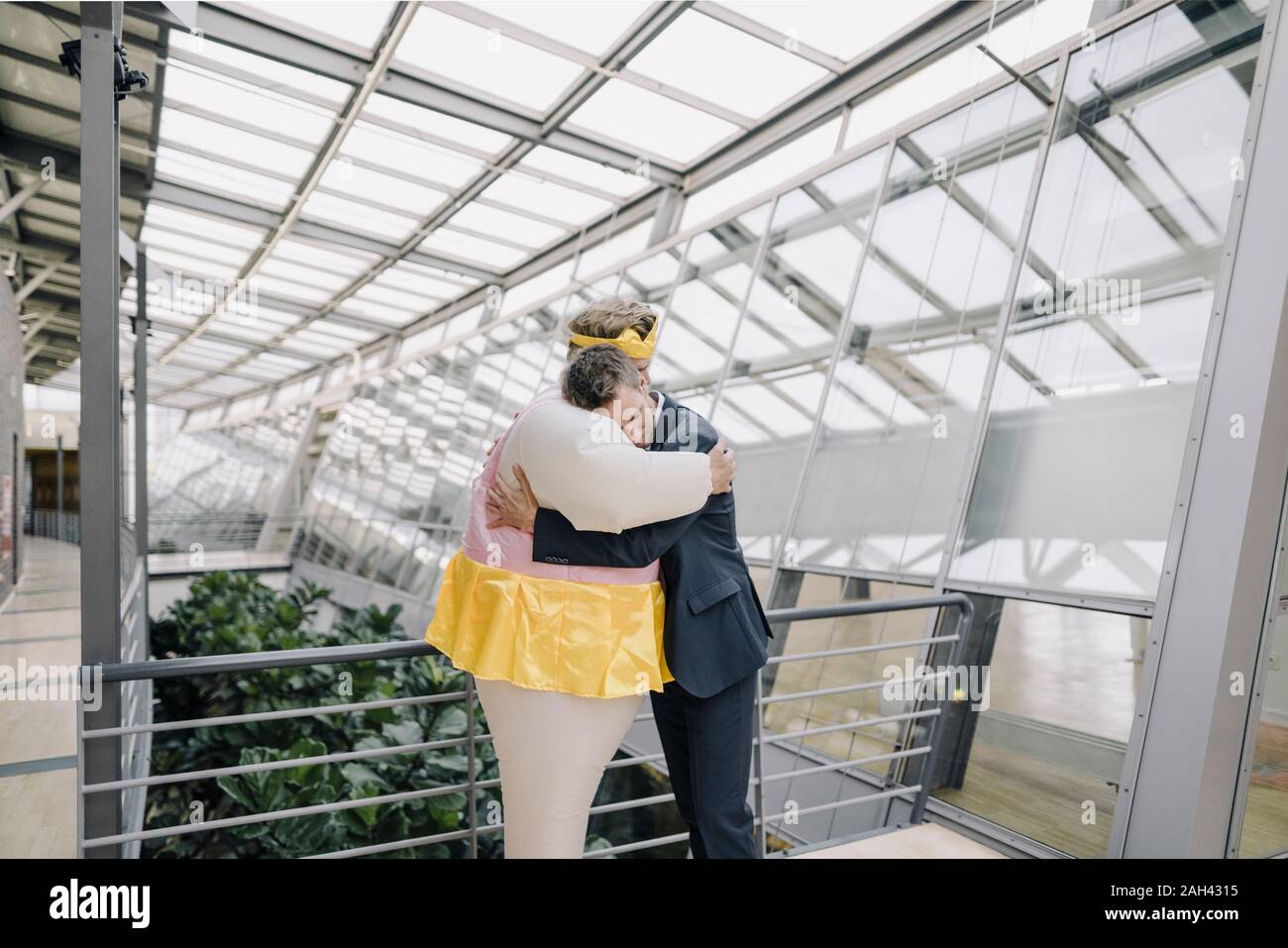 Businessman and man dressed up as a ballerina hugging in modern office building Stock Photo