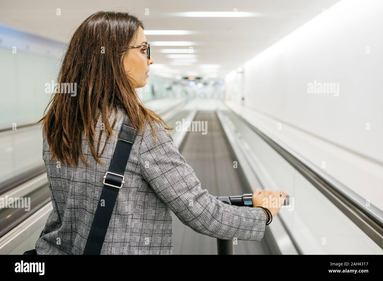 Businesswoman with her electric scooter on moving walkway Stock Photo