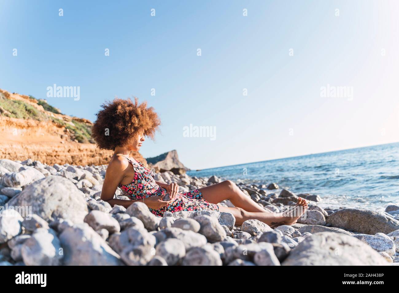 Young woman wearing summer dress and sitting on stony beach Stock Photo ...