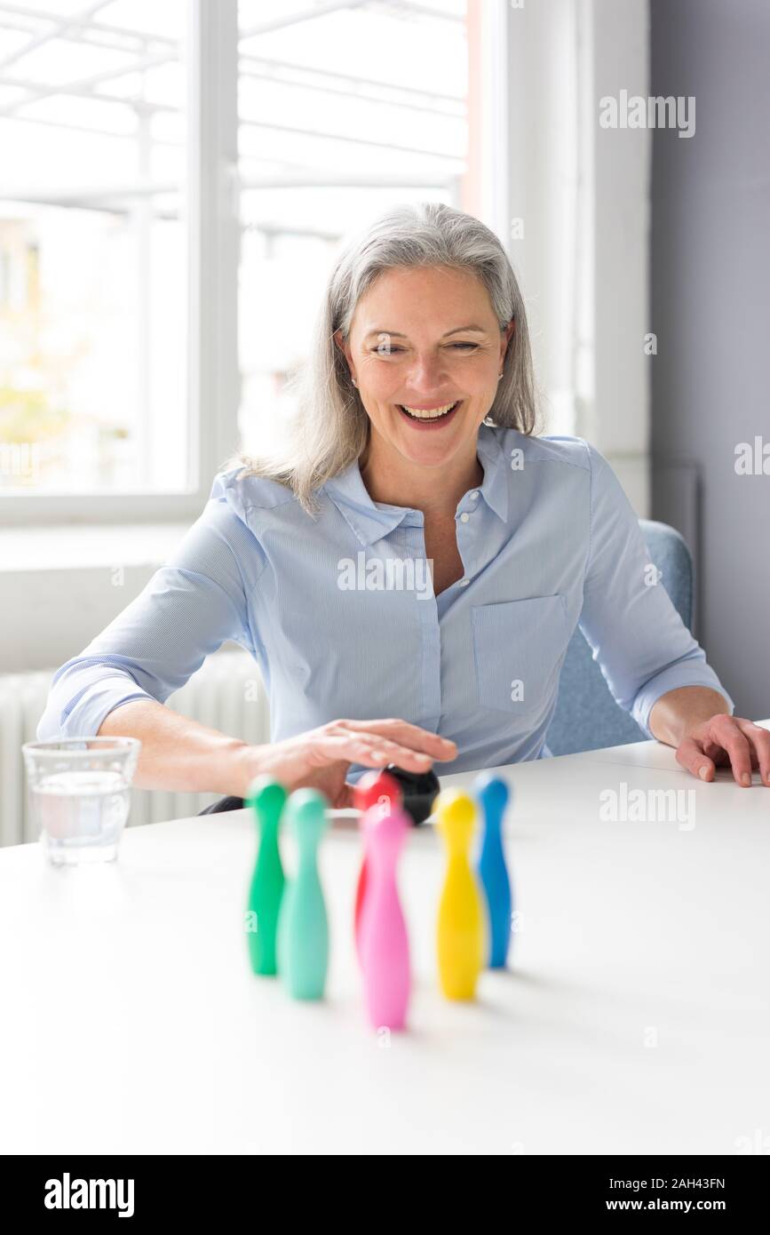 Laughing mature businesswoman playing with pins on desk in office Stock Photo