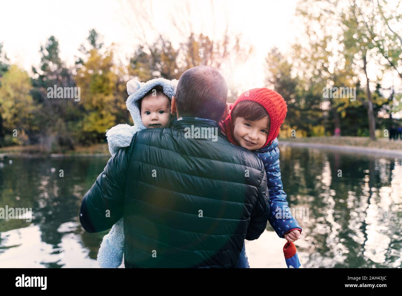 Portrait of two little girls on father's arms in front of a lake at sunset Stock Photo
