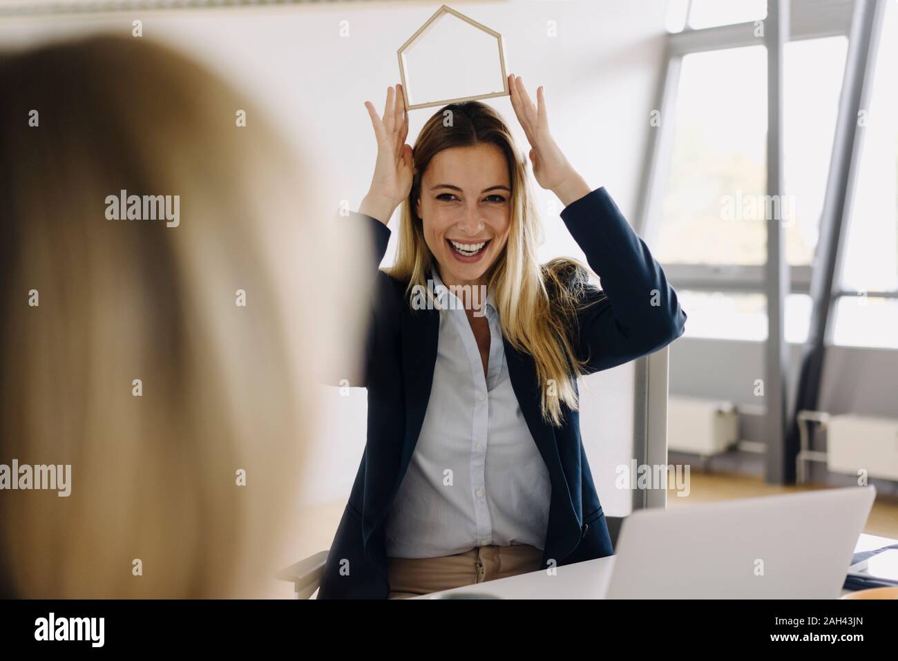 Happy young businesswomen showing house model at desk in office Stock Photo