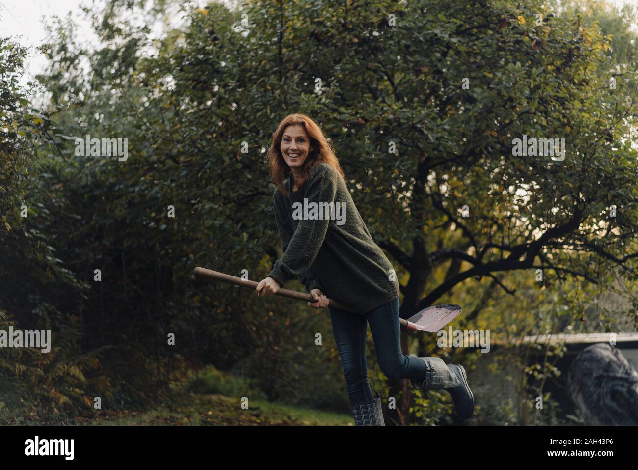 Woman working in her garden, pretending to fly on a shovel Stock Photo