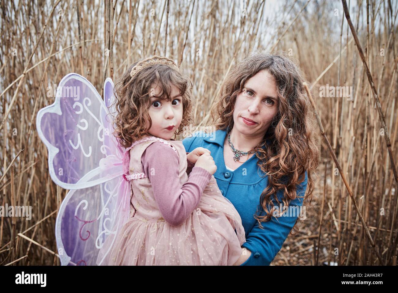Portrait of mother in nature with her little girl dressed up as a butterfly pulling funny faces Stock Photo