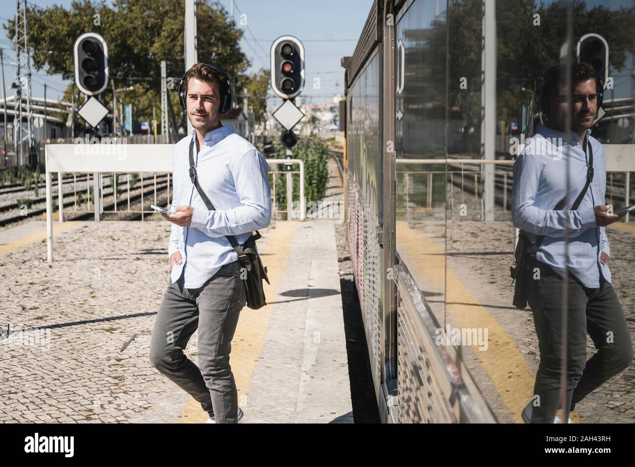 Young man with headphones and smartphone leaving train Stock Photo
