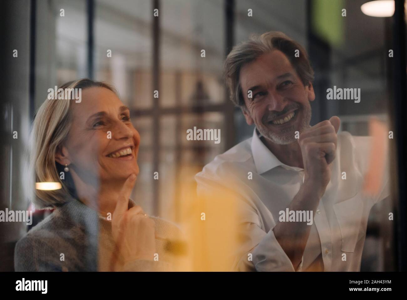 Happy businessman and businesswoman working on sticky notes at glass pane in office Stock Photo