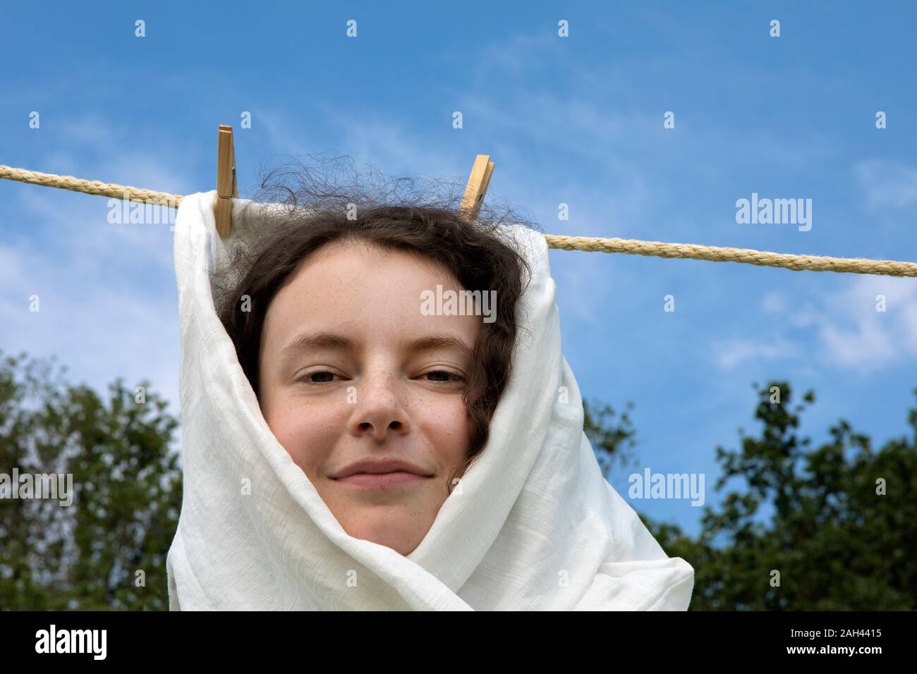 Portrait of smiling young woman wrapped in white cloth haning on clothesline Stock Photo
