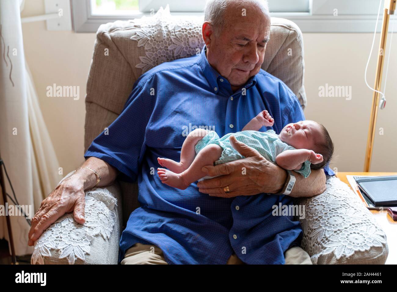Grandfather sitting in an armchair holding a newborn baby Stock Photo