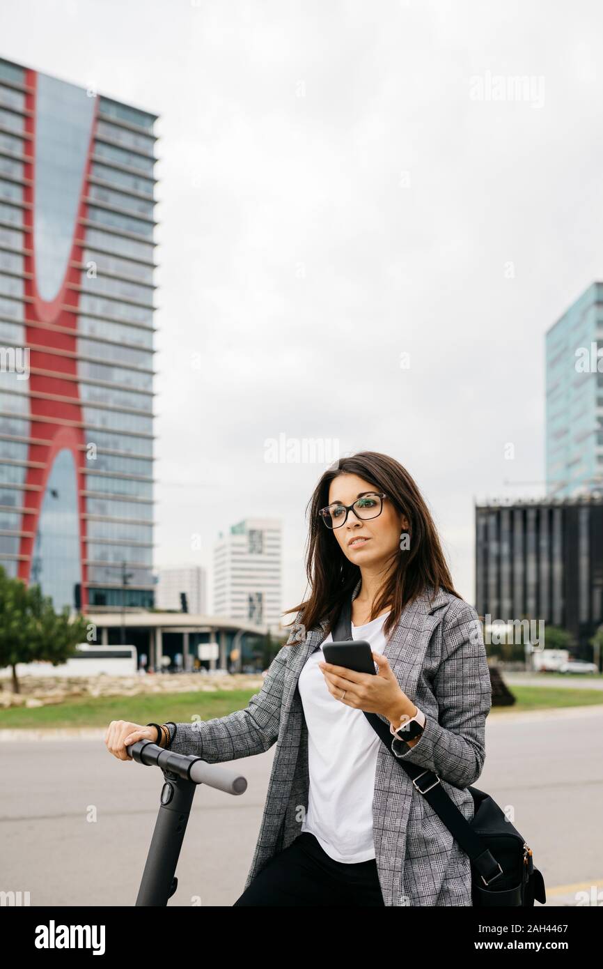 Young businesswoman using smartphone standing on e-scooter in the city Stock Photo