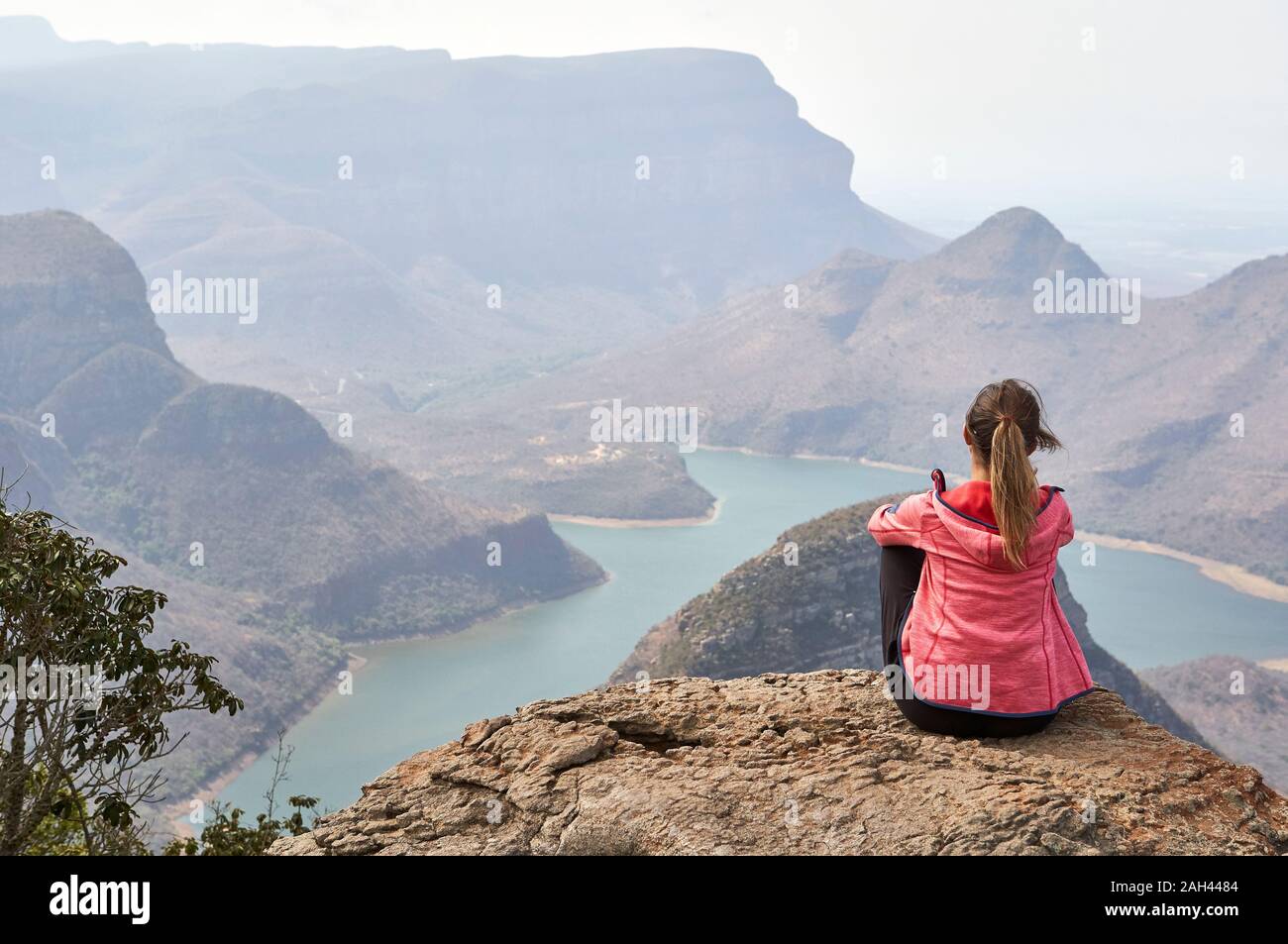 Woman sitting on a rock enjoying the beautiful landscape below her, Blyde River Canyon, South Africa. Stock Photo