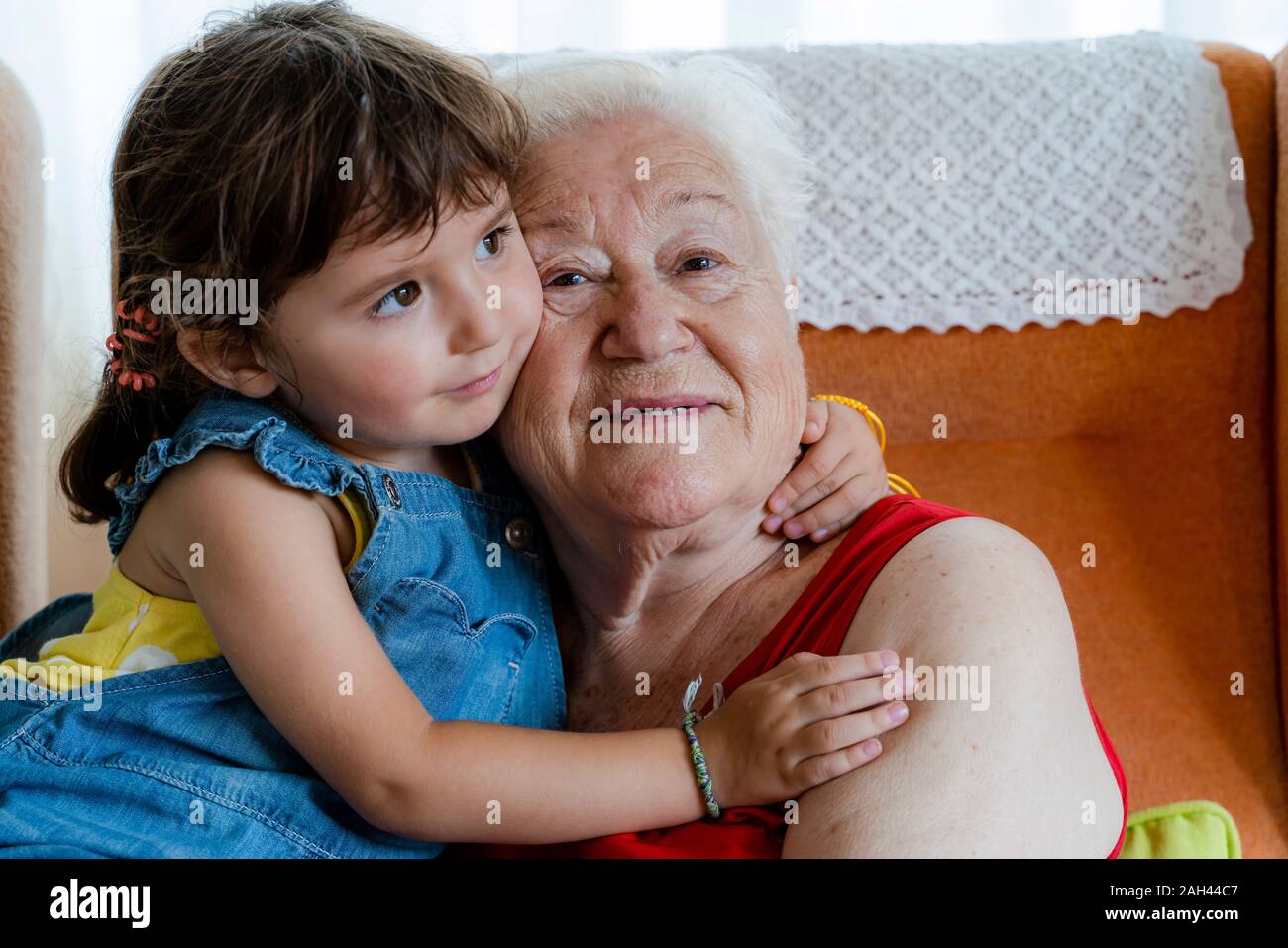 Smiling grandmother hugging her granddaughter at home Stock Photo