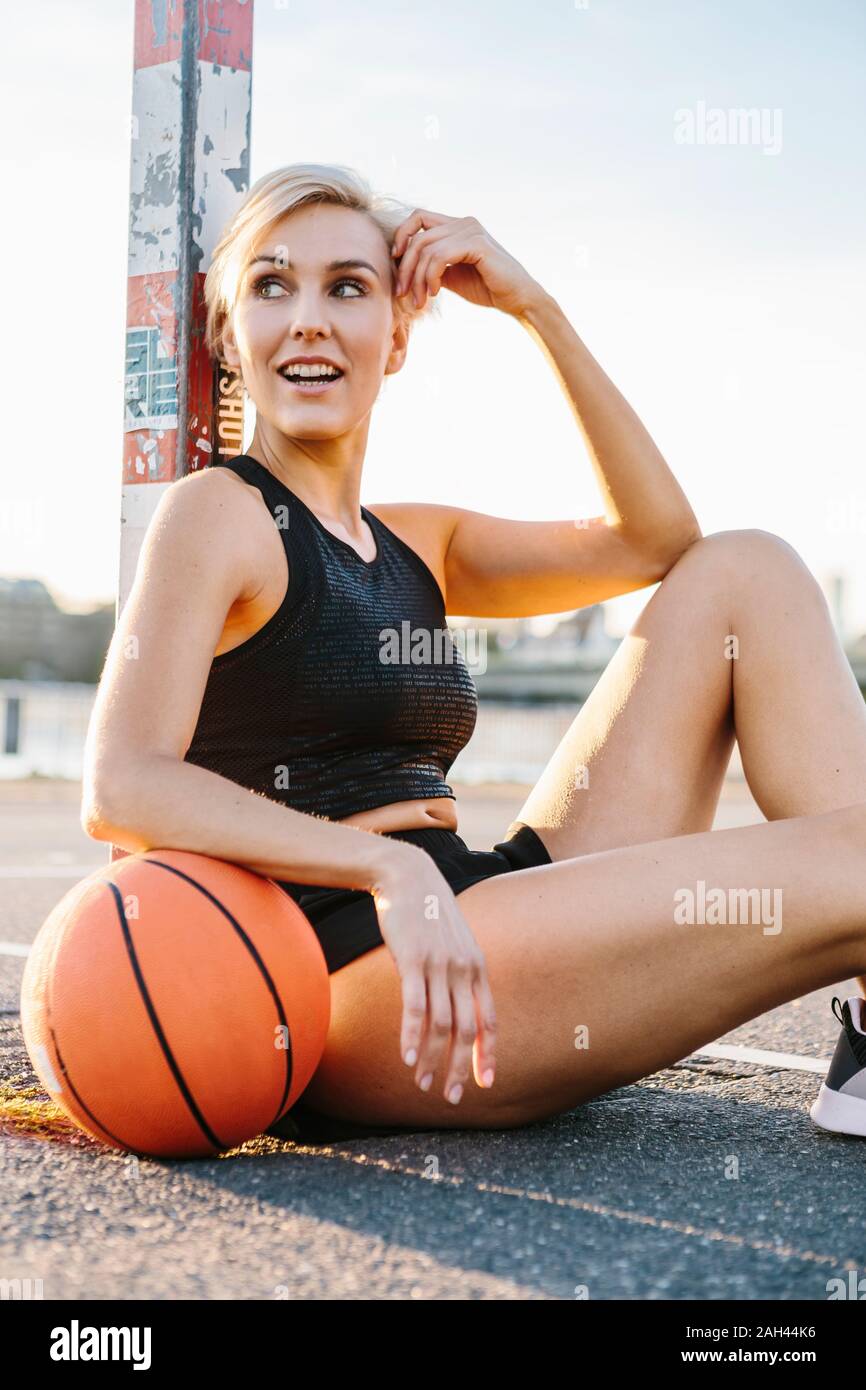 Blonde woman sitting with basketball on playing field in Cologne, Germany Stock Photo