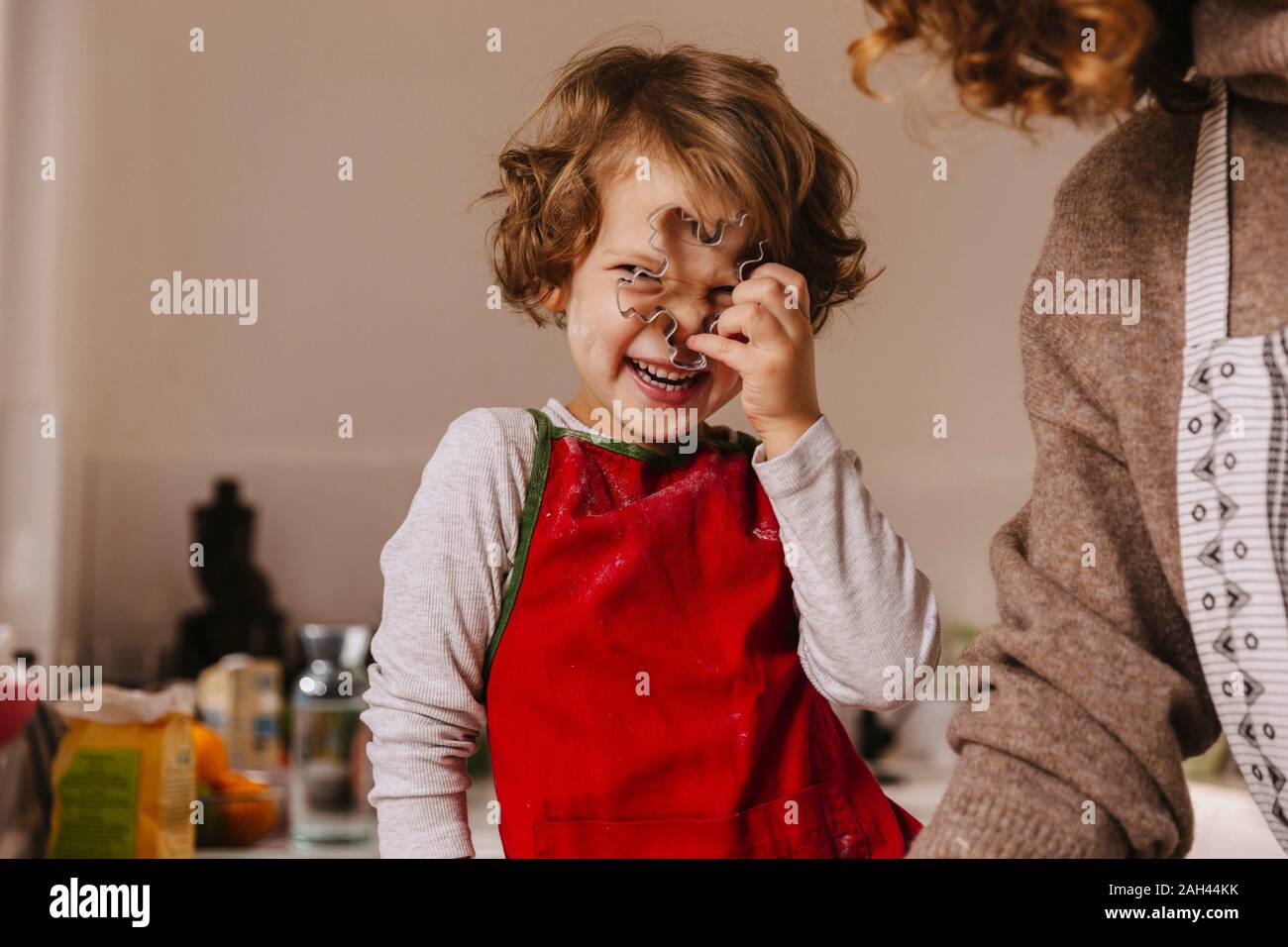Playful girl with her mother holding Christmas cookie cutter in kitchen Stock Photo