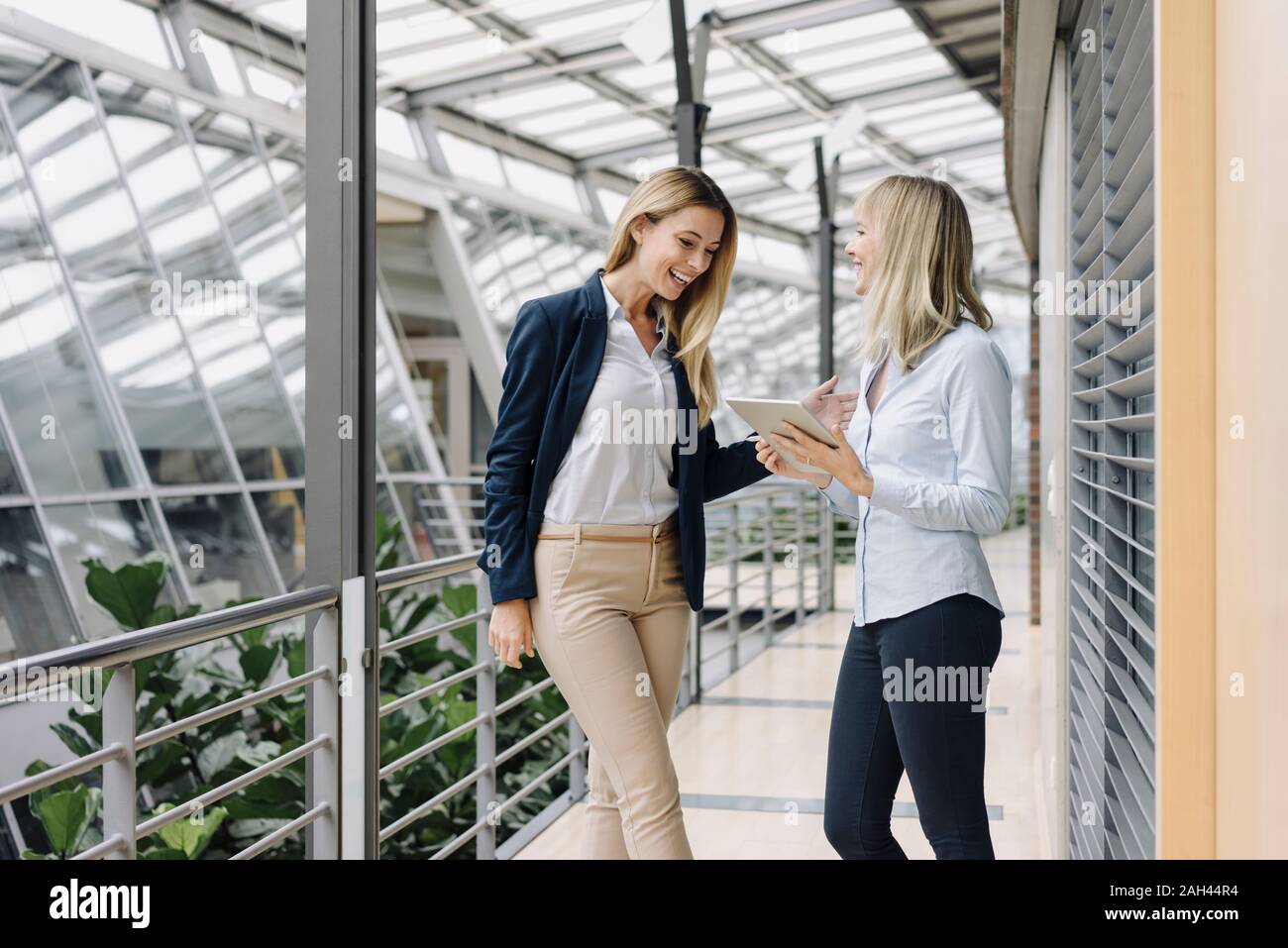 Two happy young businesswomen with tablet talking in modern office building Stock Photo