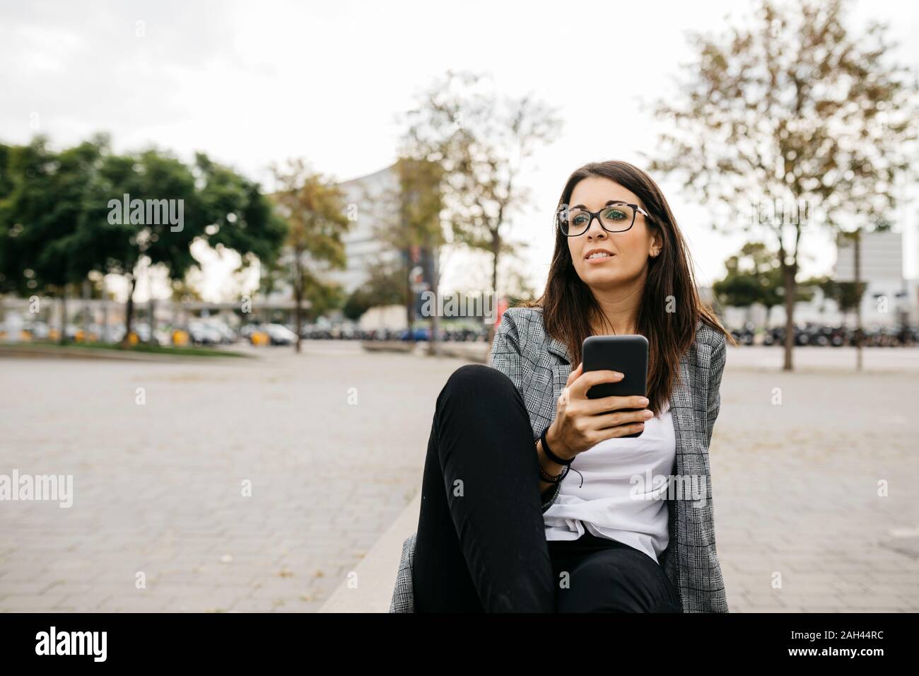 Young businesswoman using smartphone, sitting on bench in the city Stock Photo