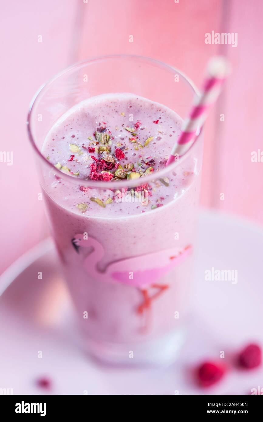 Pink vegan milkshake with raspberries, bananas, almond milk, sprinkled pistachios and dried raspberries Stock Photo