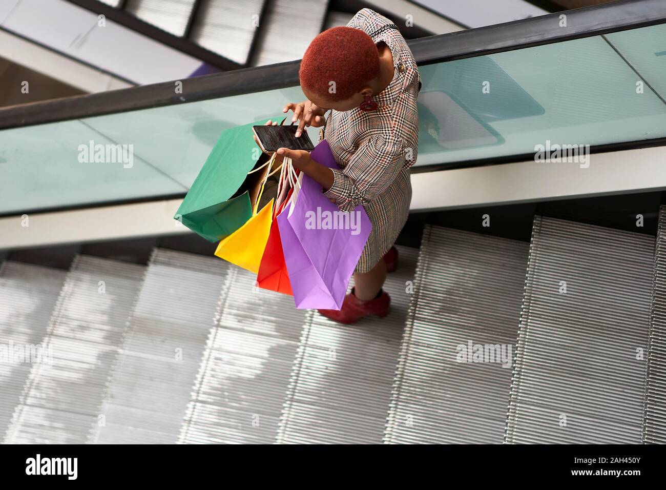 Young woman holding colorful shopping bags and checking her cell phone while descending the stairs Stock Photo
