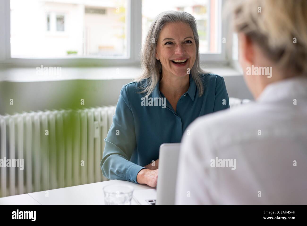 Happy mature businesswoman talking to young businesswoman at desk in office Stock Photo