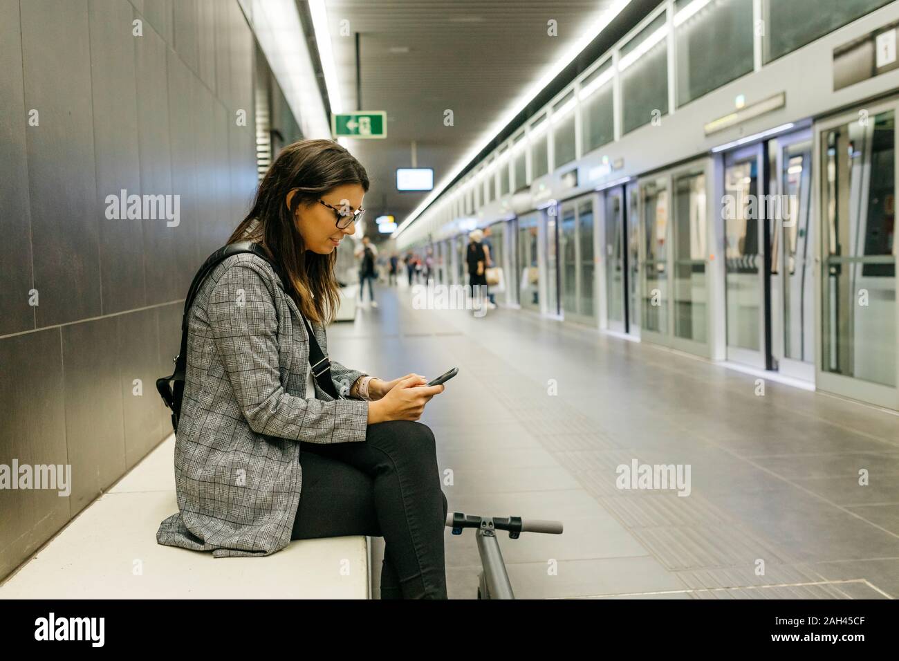 Young businesswoman with e-scooter using the phone at the subway station Stock Photo