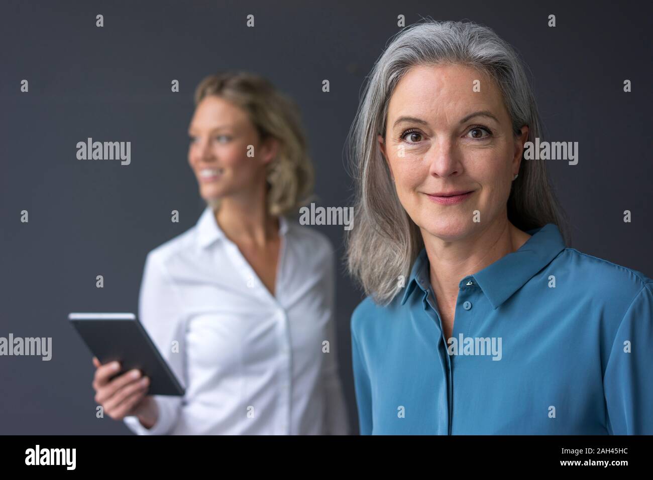 Portrait of confident mature businesswoman with young businesswoman in background Stock Photo