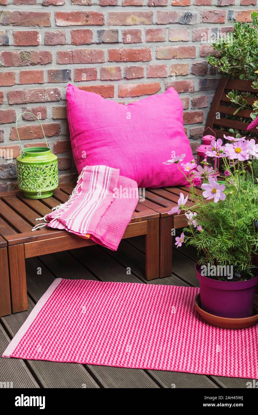 Balcony with bench, pink cushion, blanket, lantern, mat and various potted plants Stock Photo