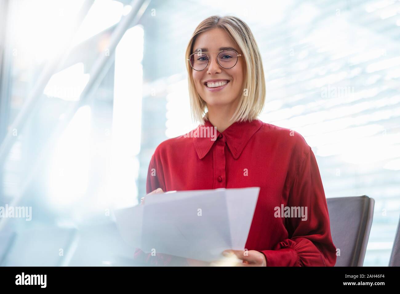 Portrait of smiling young businesswoman with papers sitting in waiting area Stock Photo