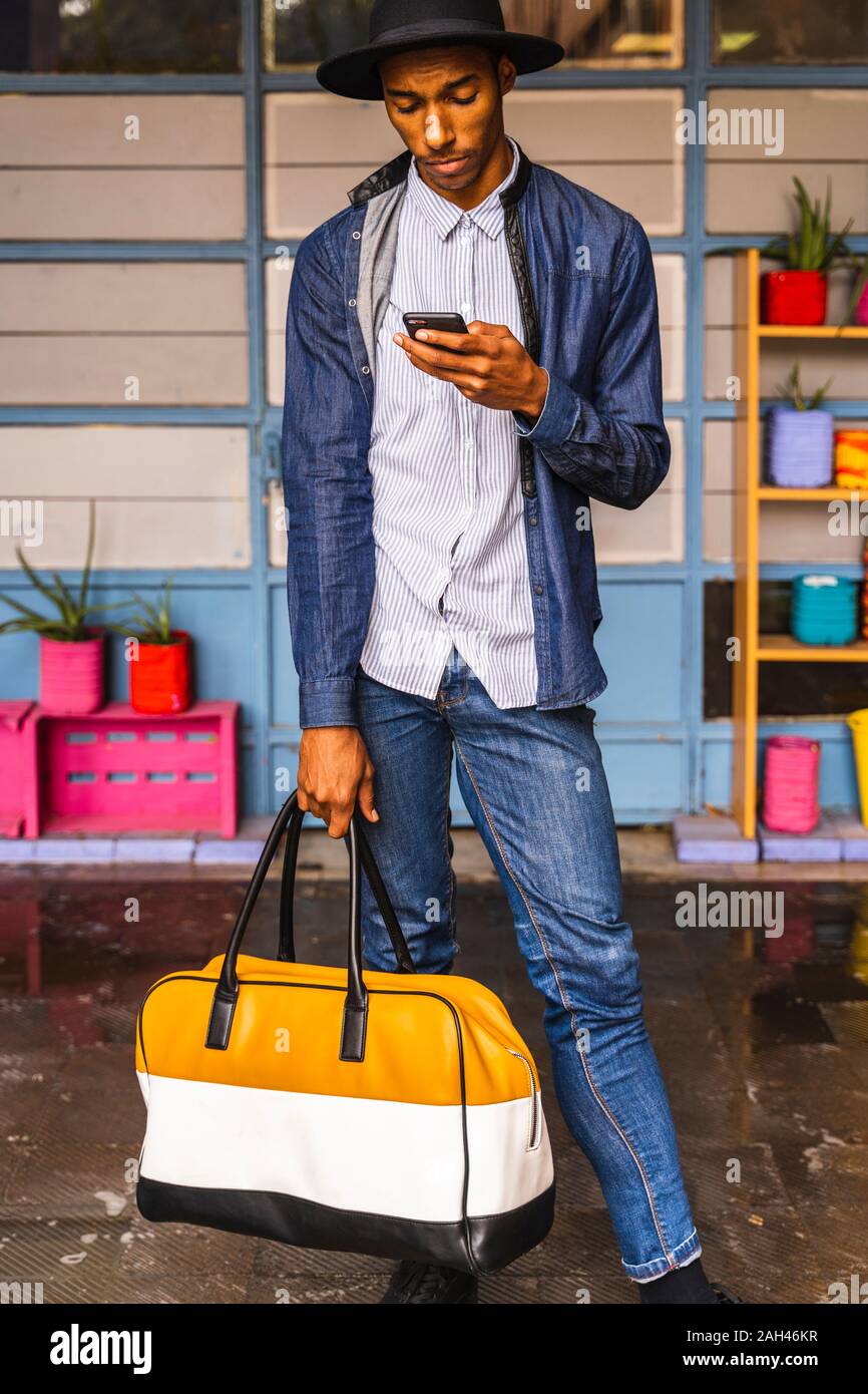 Smiling young man with bag using smartphone Stock Photo