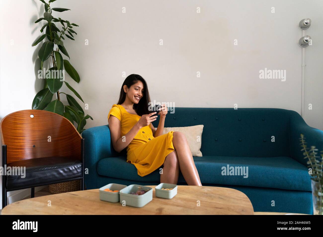 Smiling young woman sitting on couch using cell phone Stock Photo - Alamy