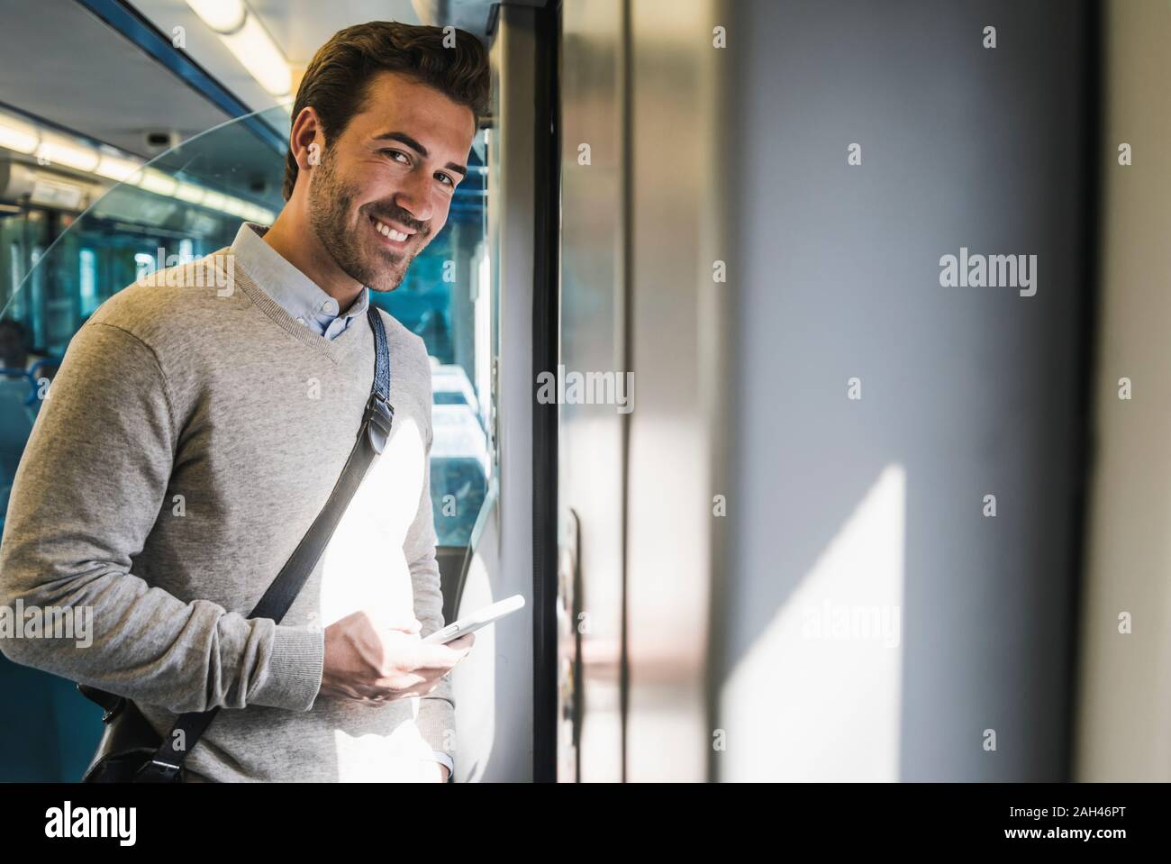 Portrait of smiling young man with smartphone on a train Stock Photo