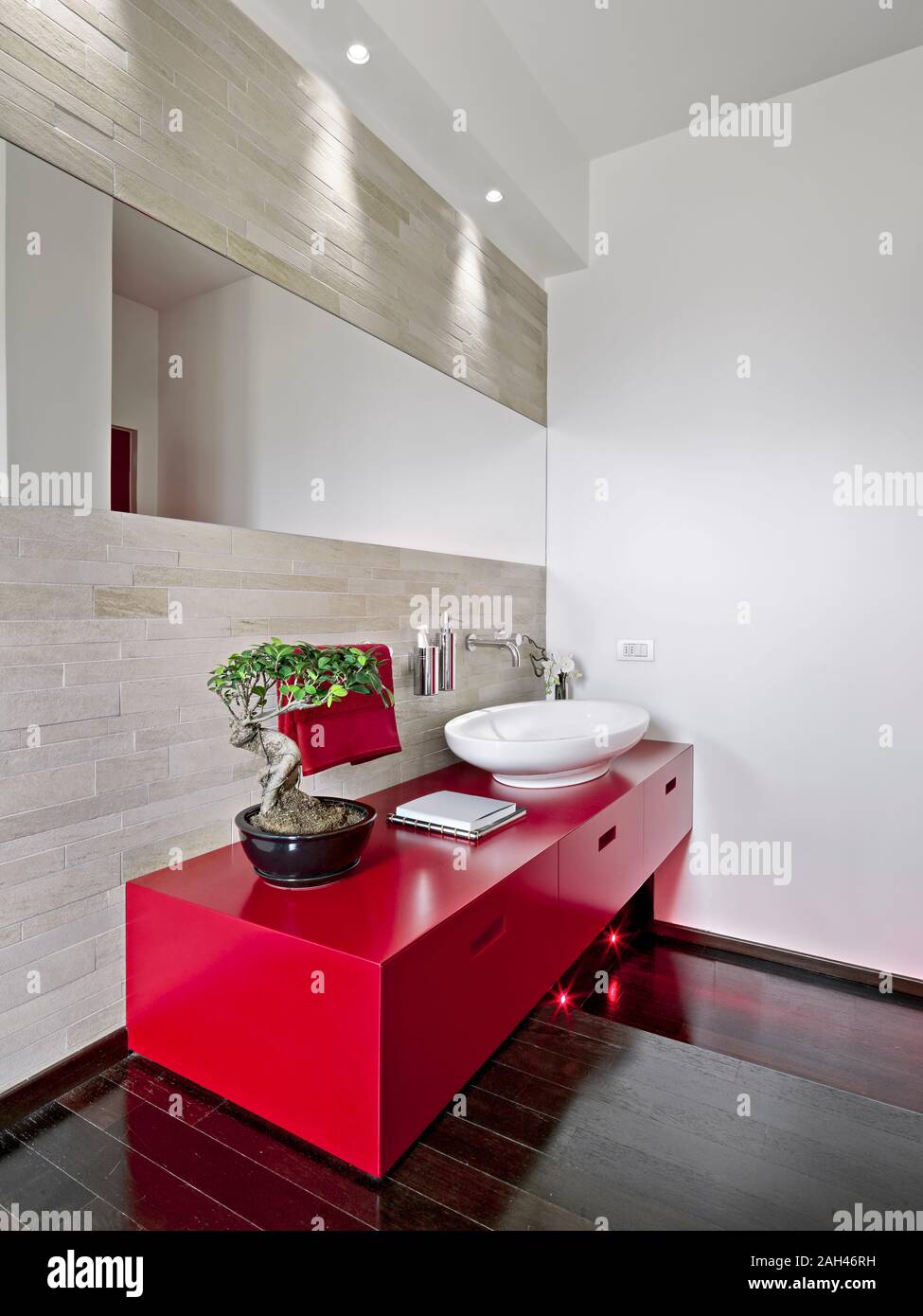 interior shot of a modern bathroom in foreground the red washbasin cabinet the floor is made of wood Stock Photo