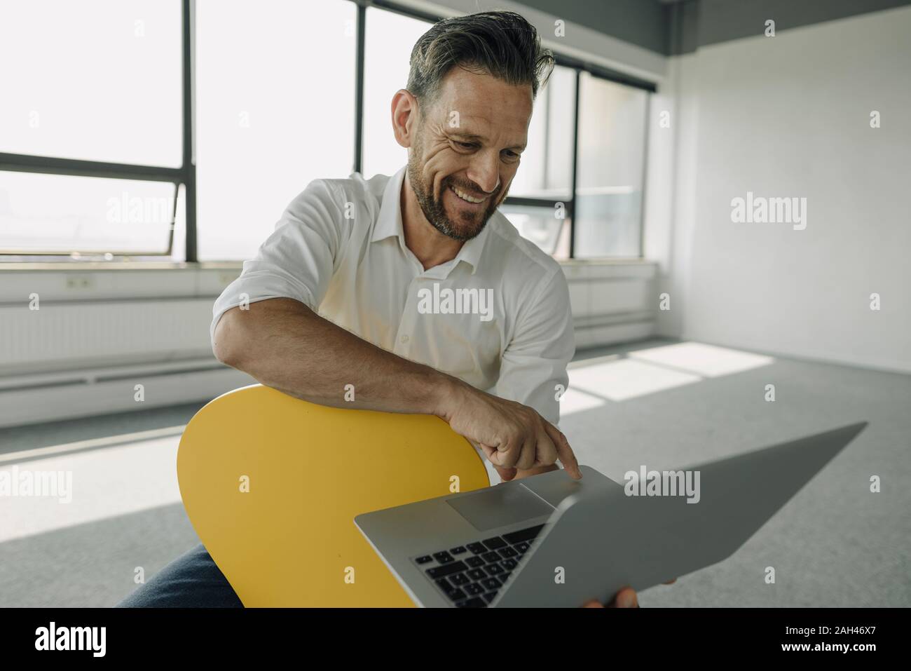 Smiling mature businessman using laptop in empty office Stock Photo