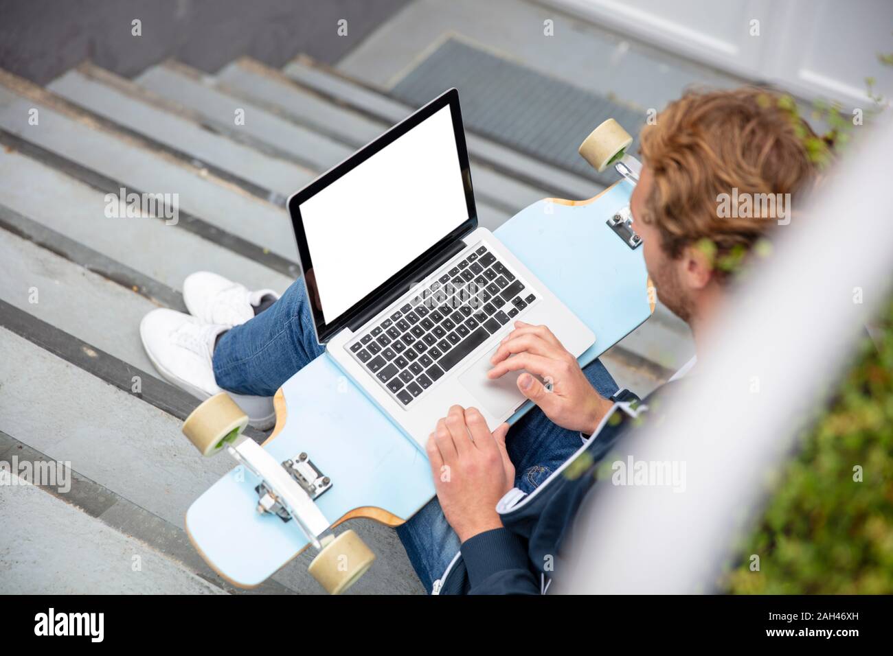 Young man sitting on steps, using laptop on longboard Stock Photo