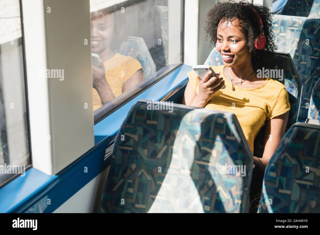 Smiling young woman with headphones and smartphone on a train Stock Photo