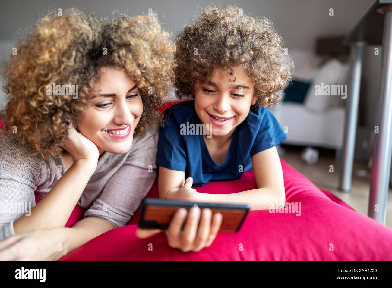 Mother and son watching a video on smartphone, lying on big pillow Stock Photo