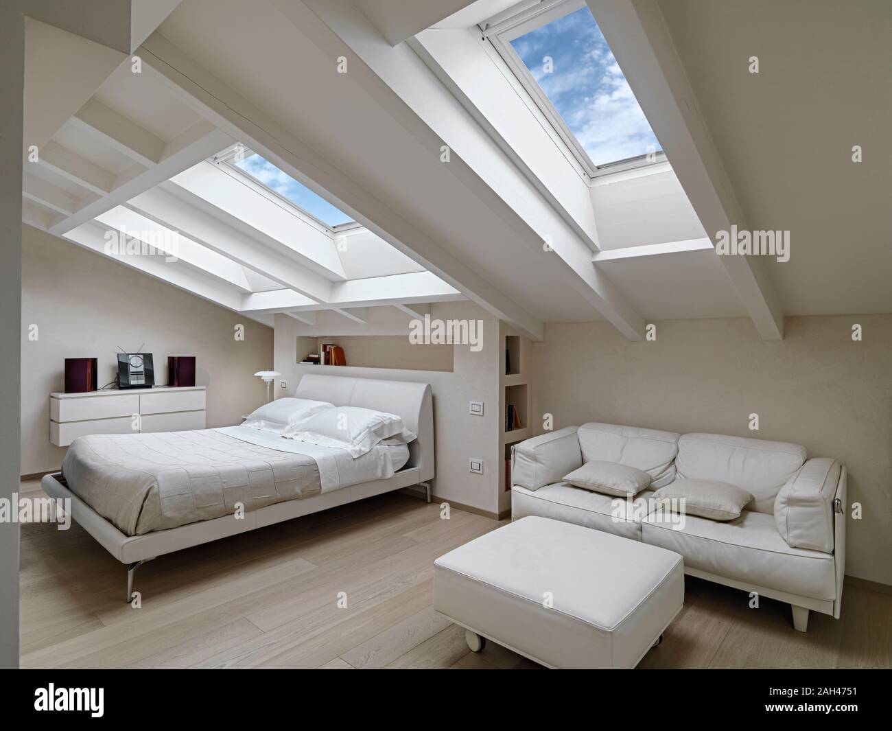 interior shot of a bedroom in the modern attic-room in the foreground the leather sofas with footrest in the background there is the bed illuminated b Stock Photo