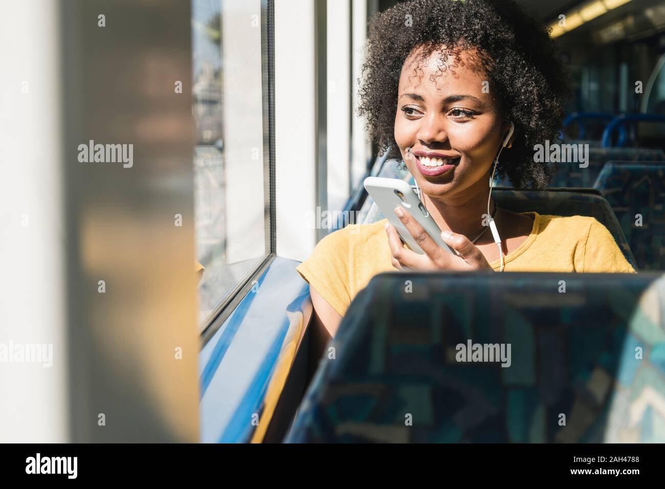 Smiling young woman with earphones and smartphone on a train Stock Photo