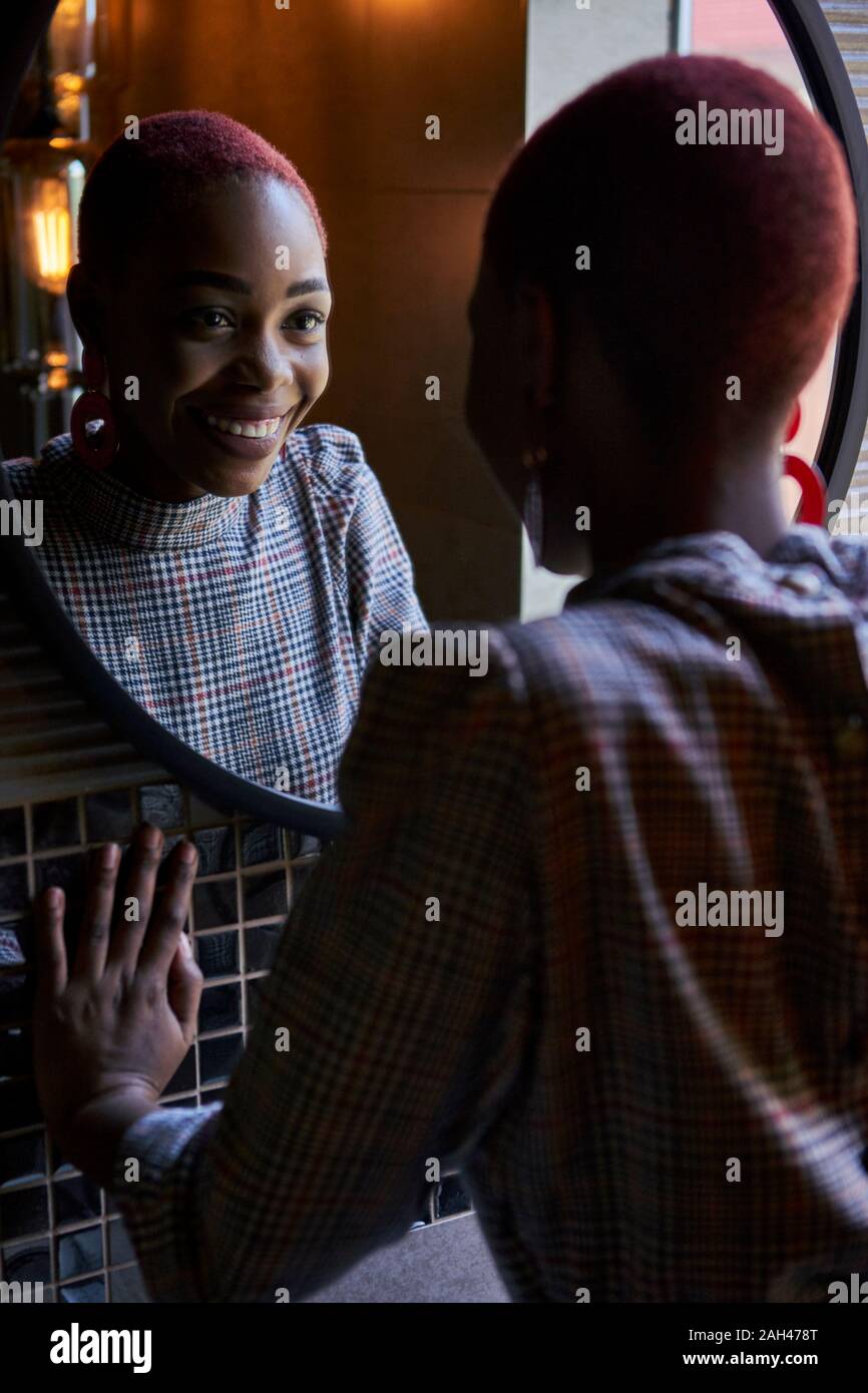 Young woman with short haircut looking and smiling to her reflection in a round mirror Stock Photo