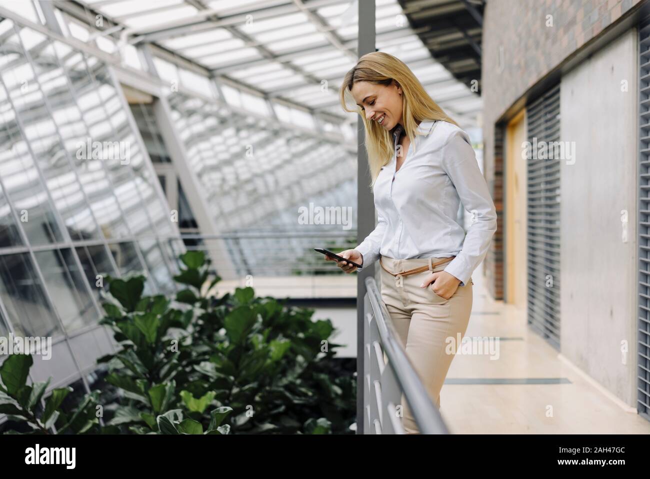 Smiling young businesswoman using cell phone in a modern office building Stock Photo