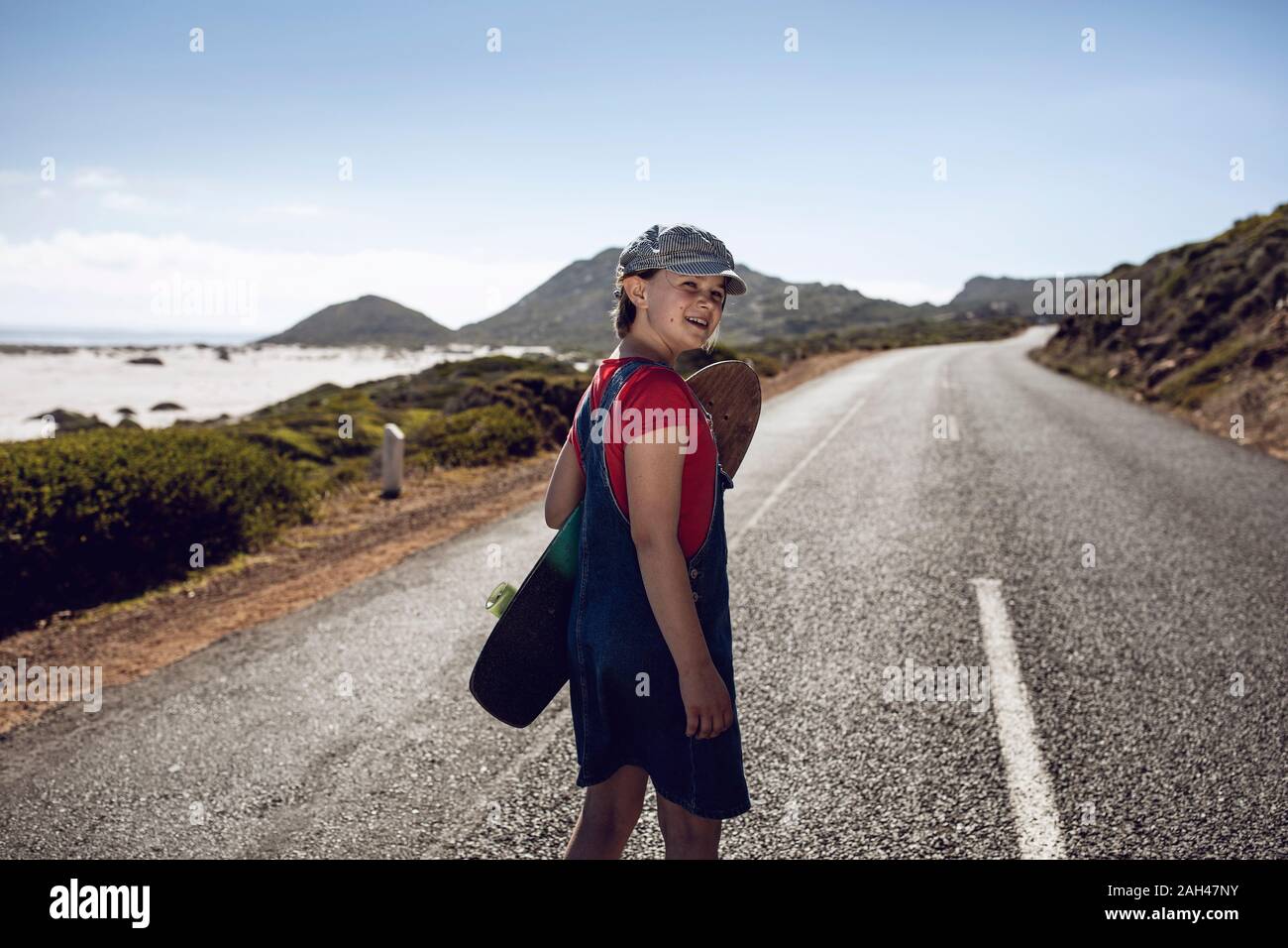 Portrait of smiling girl with skateboard standing on country road, Cape Town, Western Cape, South Africa Stock Photo