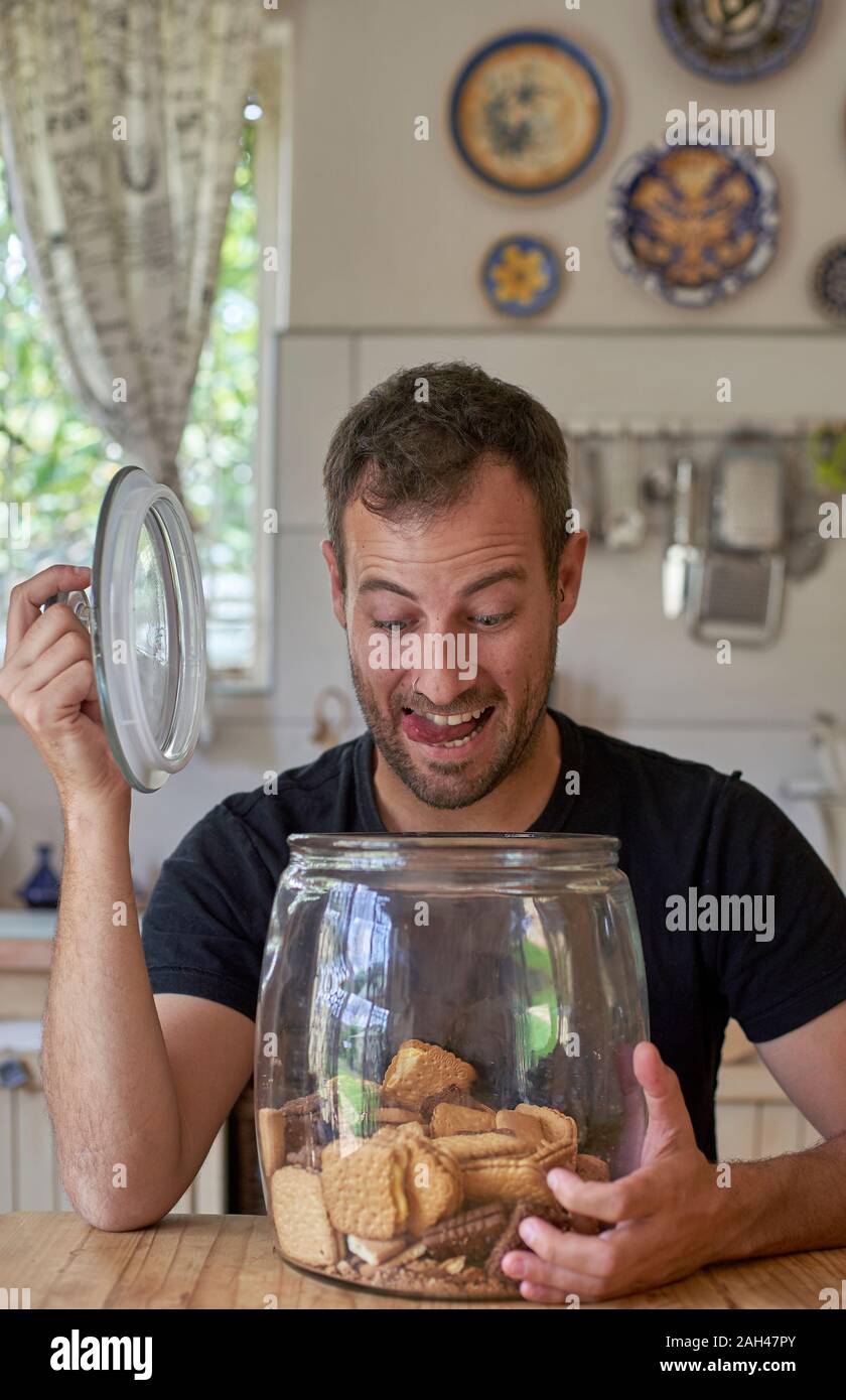 Man sitting in kitchen, looking in cookie jar, laughing Stock Photo
