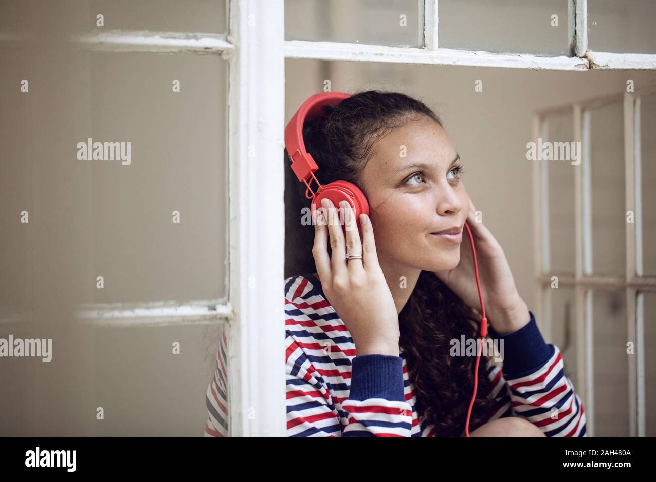 Young woman at the window listening to music Stock Photo